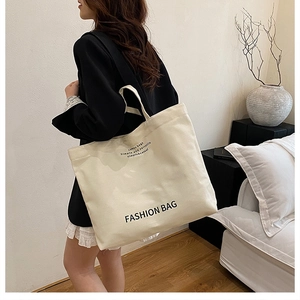 Lifestyle shot showing a large cream canvas tote bag with black lettering on a model