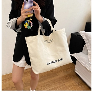 Detail showing the thick canvas texture and black letter slogan on the beige tote bag
