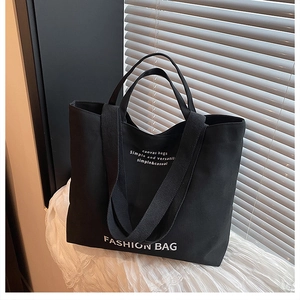 Detail of black canvas tote bag with white fashion lettering and sturdy shoulder straps
