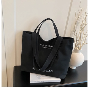 Detailed macro view of black canvas tote bag with white lettering and durable handles