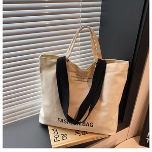 Canvas tote bag with black shoulder straps and letter print shown in a bright window scene