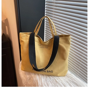 Detail of yellow canvas tote bag with black strap handles and fashion lettering print