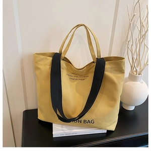 Detail of yellow canvas tote bag with black handles on a modern minimalist desk