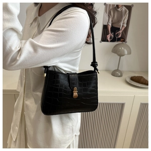 Detail of black crocodile texture shoulder bag with gold metal buckle on a model