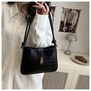 Detail of black crocodile pattern shoulder bag with a gold clasp on a model