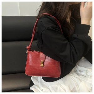 Detail of dark red underarm bag with crocodile pattern and gold metallic buckle