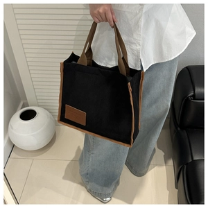Detail of black corduroy tote bag showing contrast brown handles and leather brand patch