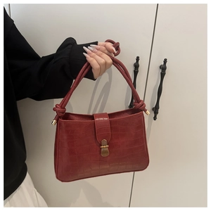 Detail view of red crocodile pattern shoulder bag with a vintage metal lock and knot handle