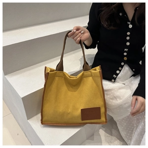 Detail of yellow waffle texture fabric tote bag with brown woven handles and leather patch