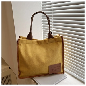 Close-up of yellow corduroy tote bag with brown straps and fashion leather label