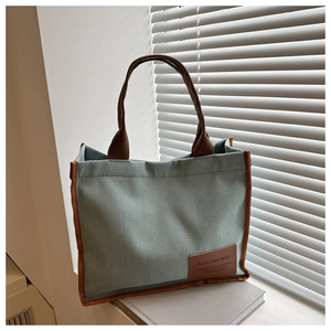 Detail of mint green waffle knit tote bag featuring contrast brown leather handles and logo