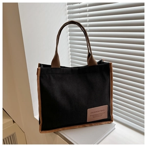 Detail of black corduroy tote bag with brown handles and fashion label in natural lighting