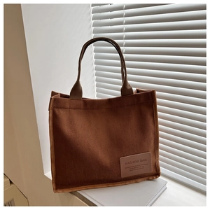 Detail of a large corduroy tote bag with leather logo tag on a white shutter background
