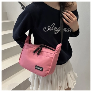 Pink nylon crossbody bag with black zippers and adjustable strap worn by a model