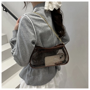 Mini transparent brown shoulder bag with gold chain strap worn by a model on stairs
