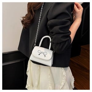 White mini bow handbag with metallic chain strap shown in a modern lifestyle setting