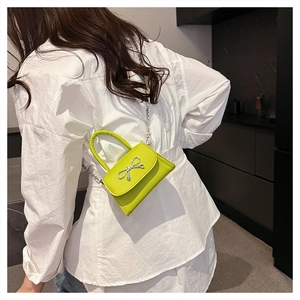 Detail of neon green mini bag with silver bow clasp and metal chain on a model