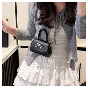 Detail of black PU leather mini handbag featuring a silver metallic bow and chain strap