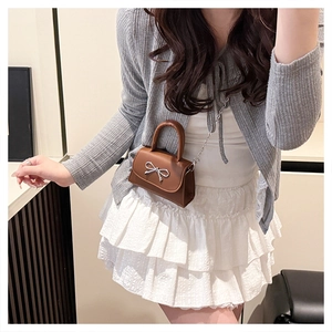 Detail of a brown mini crossbody bag with a silver bow decoration and metal chain strap