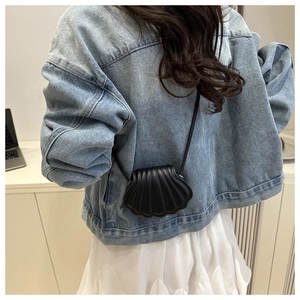 Detail shot of a black shell-shaped mini crossbody bag with pleated texture on denim jacket
