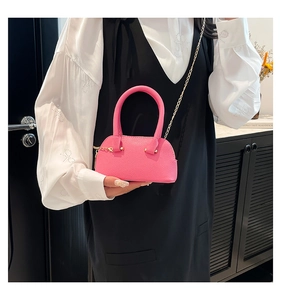Detail of bright pink shell bag with lychee texture and gold chain strap shown on model