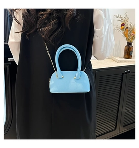Detail of light blue pebble leather shell bag with gold chain strap on black dress