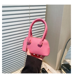 Detail of pink lychee leather mini shell bag with gold chain strap held by model