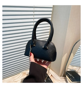 Detail of black shell-shaped tote bag showing lychee grain leather and gold chain strap