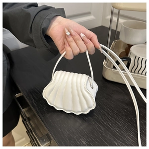 Detail of a white mini shell bag made of smooth PU leather held in hand for scale