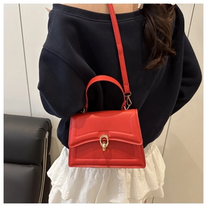 Red crossbody bag with gold ring buckle shown on a model wearing white pleated skirt