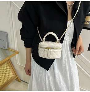 Detail shot of a white quilted box bag featuring a golden chain strap on a model