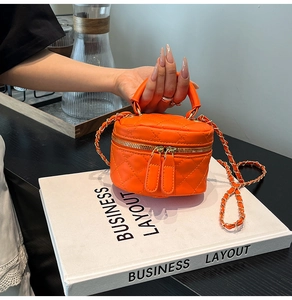 Detail of orange quilted cylinder bag with gold chain strap and textured PU leather