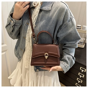 Detail of dark brown leather crossbody bag with gold ring buckle and top handle