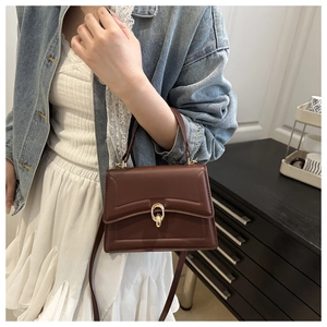 Detail shot of brown leather handbag featuring a golden ring clasp and adjustable strap