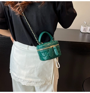Detail of green quilted mini box bag with gold chain strap worn by a fashion model
