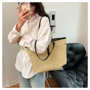 Detailed texture of large woven straw tote bag with black leather shoulder straps