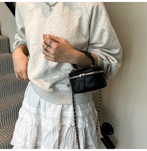 Detail of a mini black quilted box bag with a gold chain strap worn on a crossbody