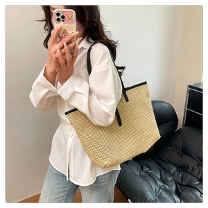 Mirror selfie showing the large woven straw tote bag with black leather straps and trim