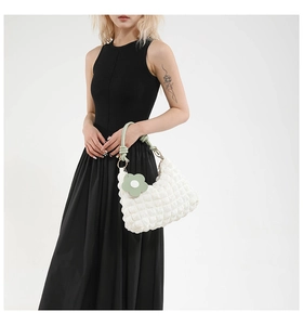 Detail of white bubble texture handbag with green woven handle and flower charm