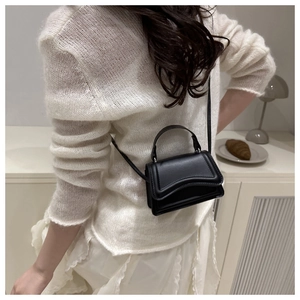 Detail of a black mini leather square bag featuring a unique wavy edge flap and slim strap