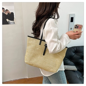 Detail of a straw woven tote bag featuring black leather handles and high-quality texture
