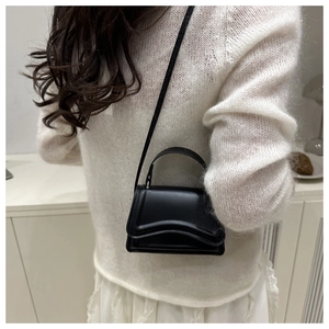 Detail view of mini black crossbody bag with wavy flap design on white knit outfit