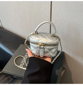 Close-up of a mini silver quilted box bag with chain strap held in hand for size detail