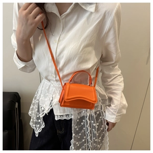 Detail of a vibrant orange leather crossbody bag with top handle and fine stitching