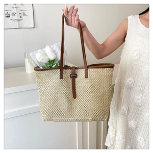 Detailed close-up of woven straw tote bag featuring brown leather handles and interior space