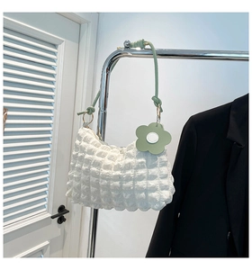 Detail of white pleated handbag with bubble texture and light green flower pendant