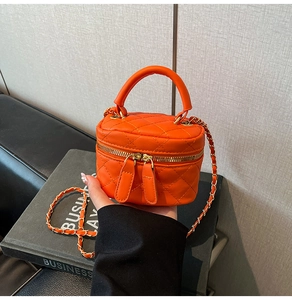 Detail of bright orange quilted mini bag with gold chain strap and dual zipper closure