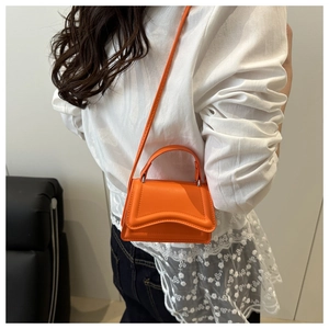 Close-up of bright orange mini leather bag featuring a stylish wave flap and shoulder strap