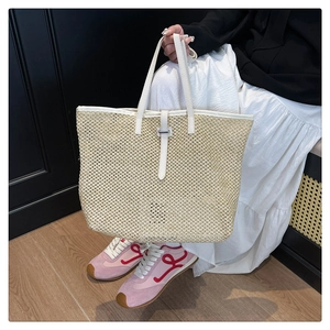 Detail of large woven straw tote bag with white faux leather trim and metallic buckle