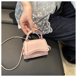 Pink mini crossbody bag held by hand showing compact size and curved flap design